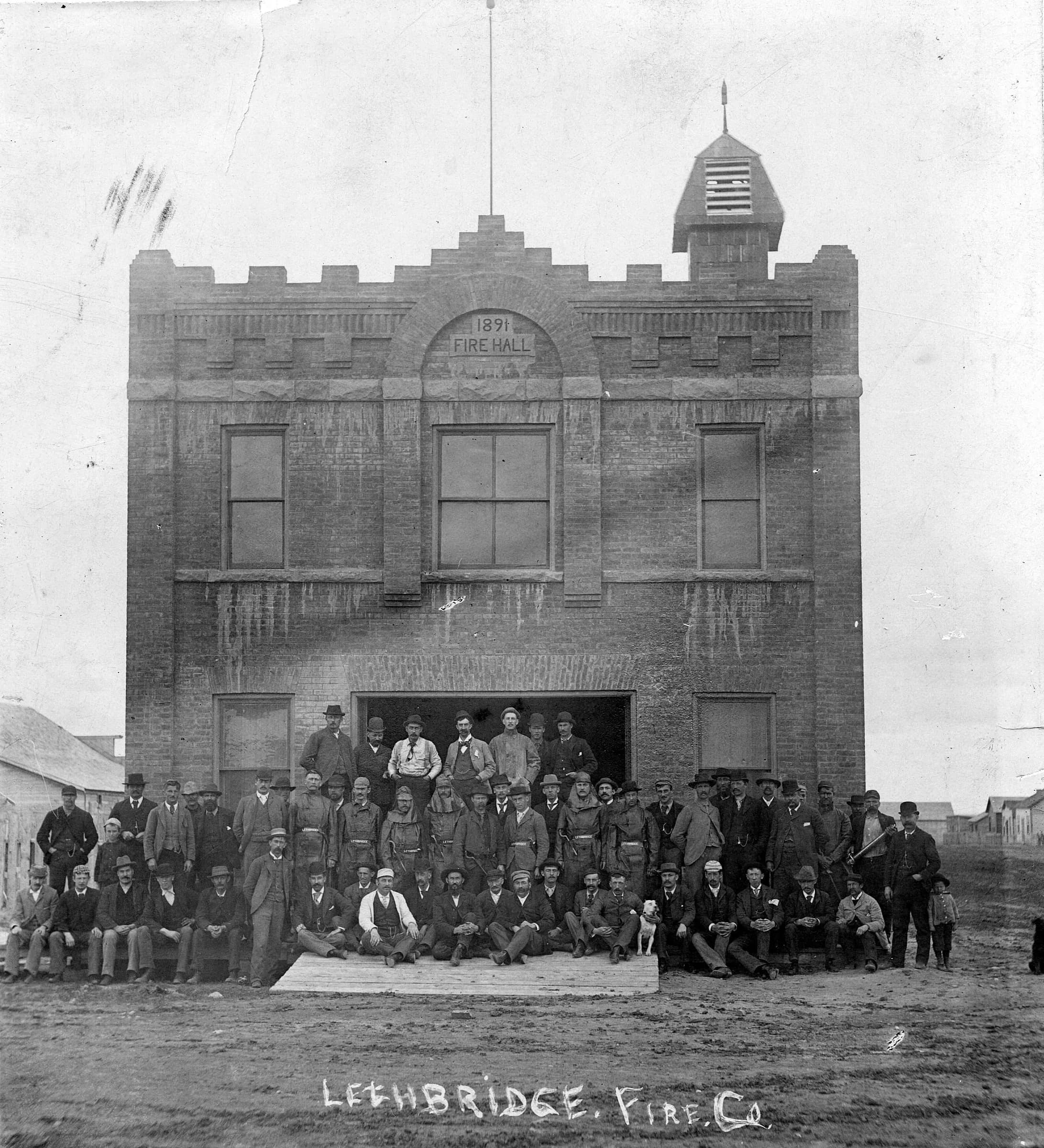 An archival Lethbridge fire-company group outside a hall labelled 1891 Fire Hall.